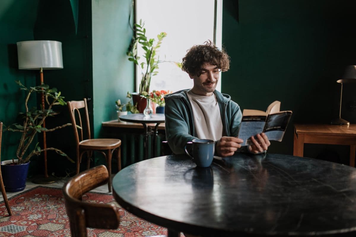 Une personne lit un livre dans un café aux murs verts et plantes